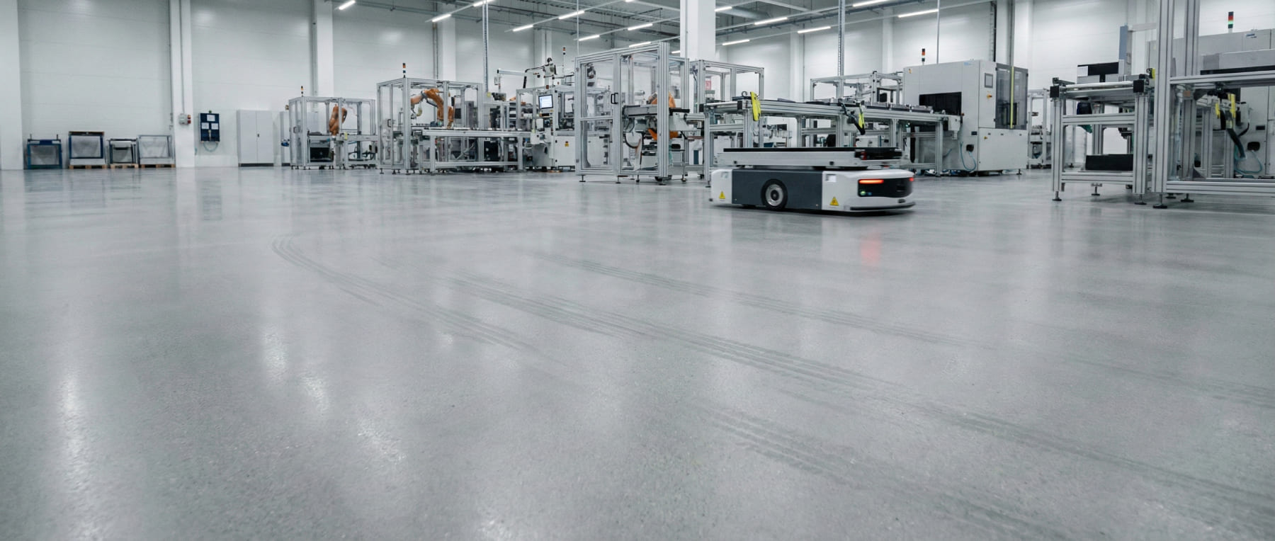 Fahrerloses Transportsystem auf leitfähigem Betonboden in einer Automobil-Produktionshalle mit Robotern im Hintergrund - Visualisierung von ESD-Schutz in der E-Mobility Fertigung.