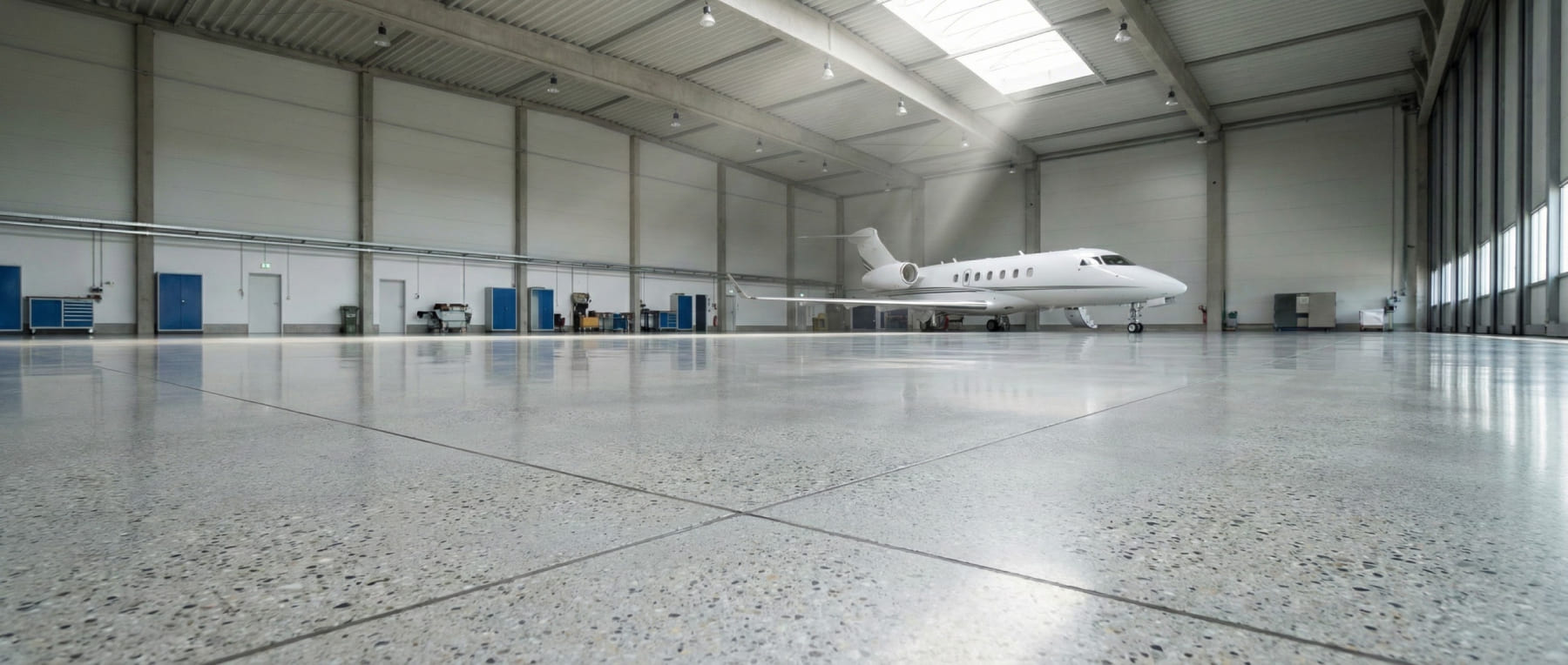 Weitwinkelaufnahme eines sterilen Flugzeughangars mit einem Business Jet auf hochglanzpoliertem Grindingfloor Betonboden - Visualisierung von Helligkeit und Skydrol-Resistenz für die Luftfahrt.
