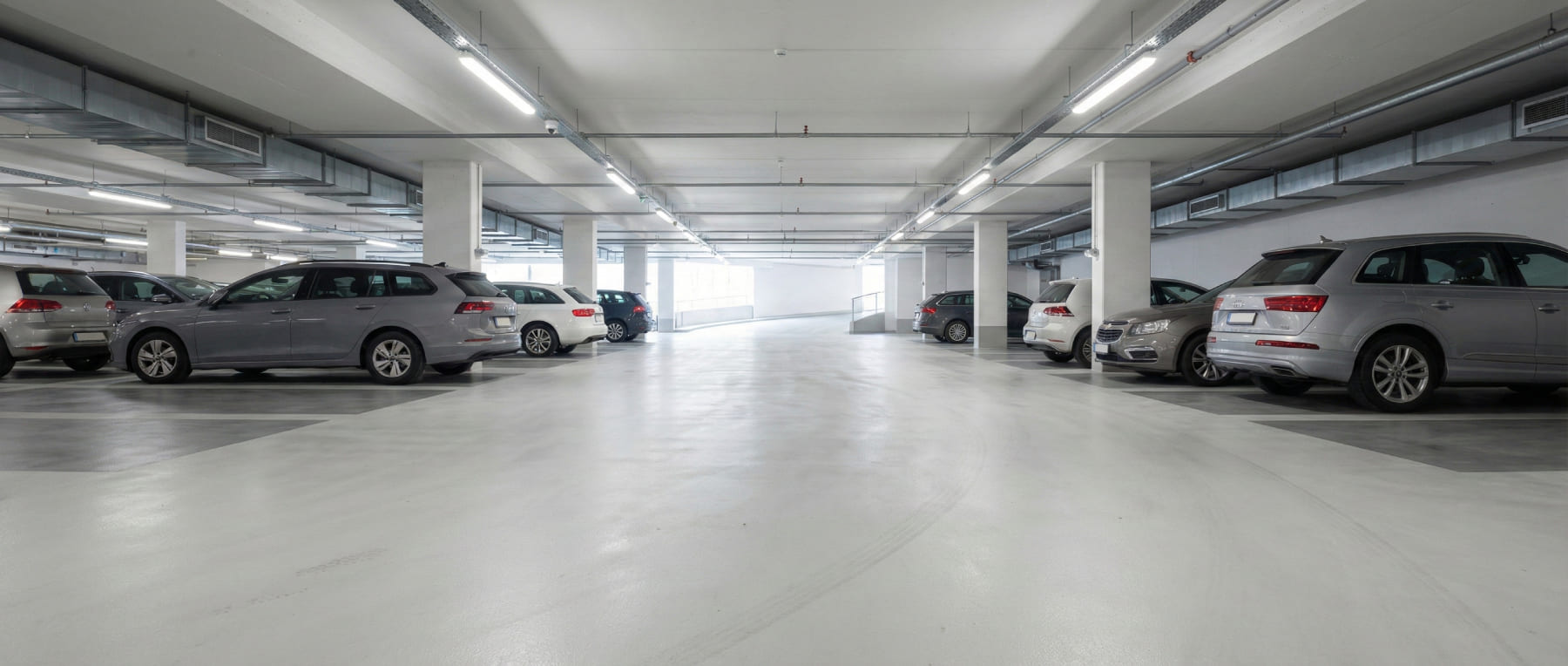 Helles und sauberes Parkdeck in einem Einkaufszentrum mit geparkten Autos auf poliertem Betonboden - Visualisierung der Parkraumsanierung für ein gesteigertes Sicherheitsgefühl.