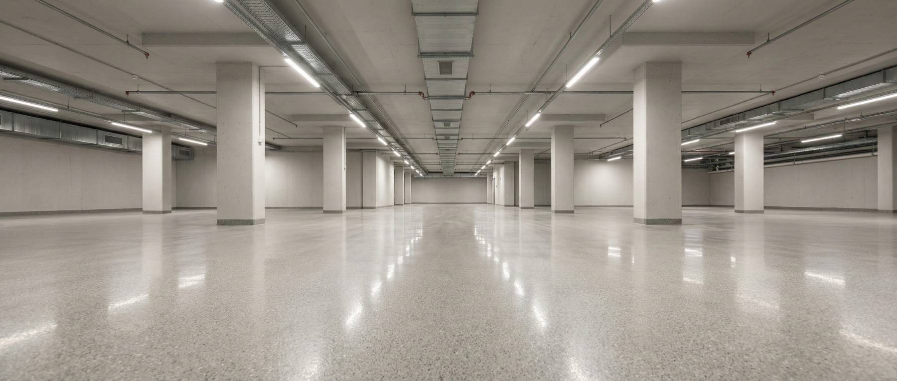Leere, extrem helle Tiefgarage mit poliertem Betonboden, der die Deckenbeleuchtung stark reflektiert - Visualisierung der erhöhten Lichtreflexion für mehr Sicherheit und Energieeffizienz.