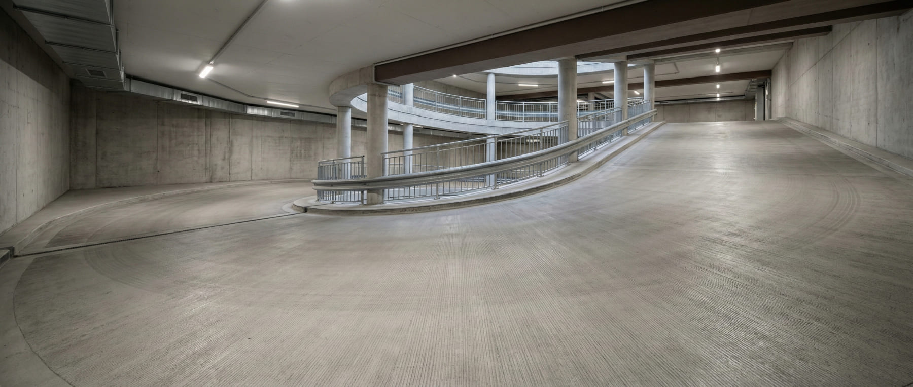 Massive Betonspindel und kurvige Auffahrt in einem Parkhaus mit Metallgeländer und strukturierter Oberfläche - Visualisierung der Sanierung von Rampen und Kurvenbereichen gegen Scherkräfte.