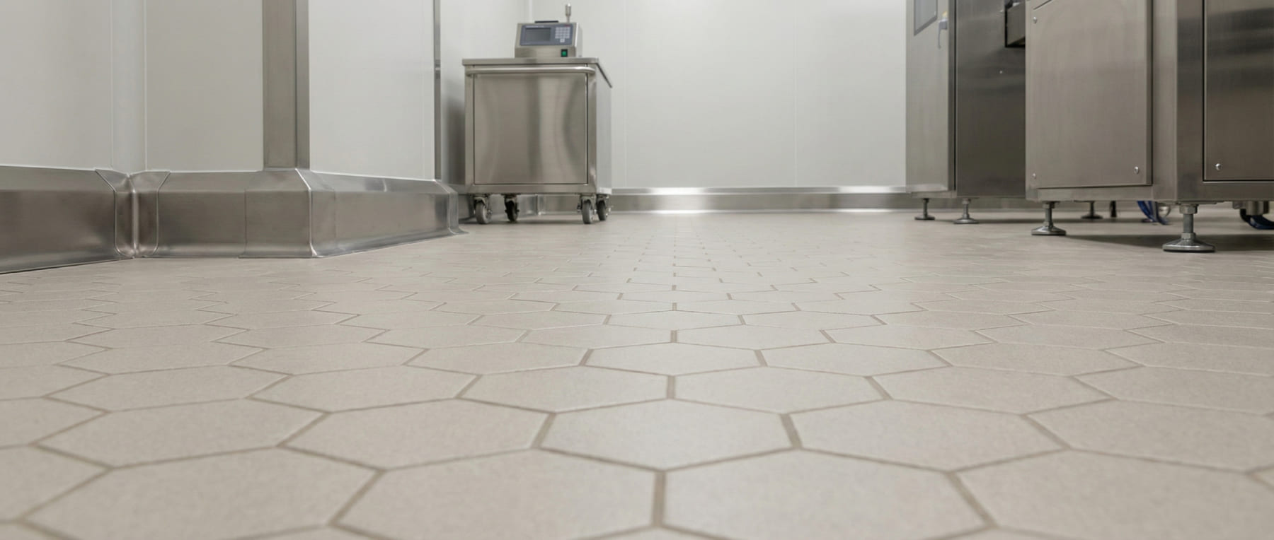 Froschperspektive eines sterilen Pharma-Produktionsraums mit geschliffenen Sechseckfliesen und Edelstahlsockeln - Visualisierung von Reinraum-Konformität nach GMP und HACCP Standards.