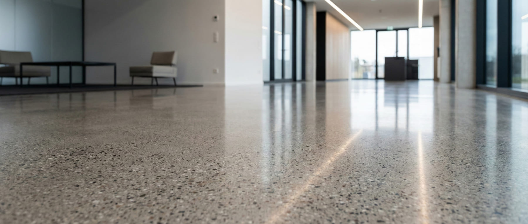 Froschperspektive eines modernen Foyers mit hochglanzpoliertem Grindingfloor Sichtestrich - starke Lichtreflexionen auf der Oberfläche und sichtbare Gesteinskörnung verdeutlichen das hochwertige Finish und Design.