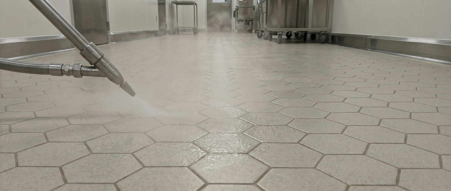 Edelstahldüse sprüht Heißdampf auf einen Boden aus Sechseckfliesen in einer sterilen Umgebung - Visualisierung der Temperaturschock-Resistenz und thermischen Belastbarkeit.